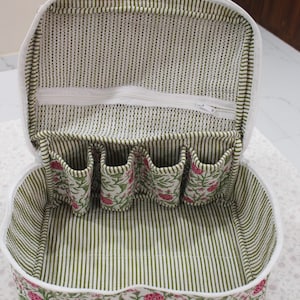 May include: Open, white-trimmed cosmetic bag with a floral print on the exterior and a green and white striped interior. The bag has a zippered top and several small pockets inside for organizing items.