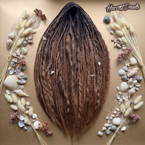 May include: A set of brown synthetic dreadlocks featuring a dark root transition, various braid textures, and small decorative charms. The text Harvest Dreads is visible in the upper right corner, surrounded by dried grasses and seashells.