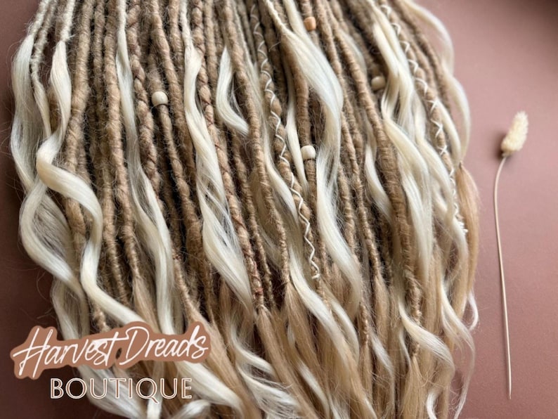 a close-up view of a collection of braided hair strands, with a small white flower or dried plant stem visible next to them.