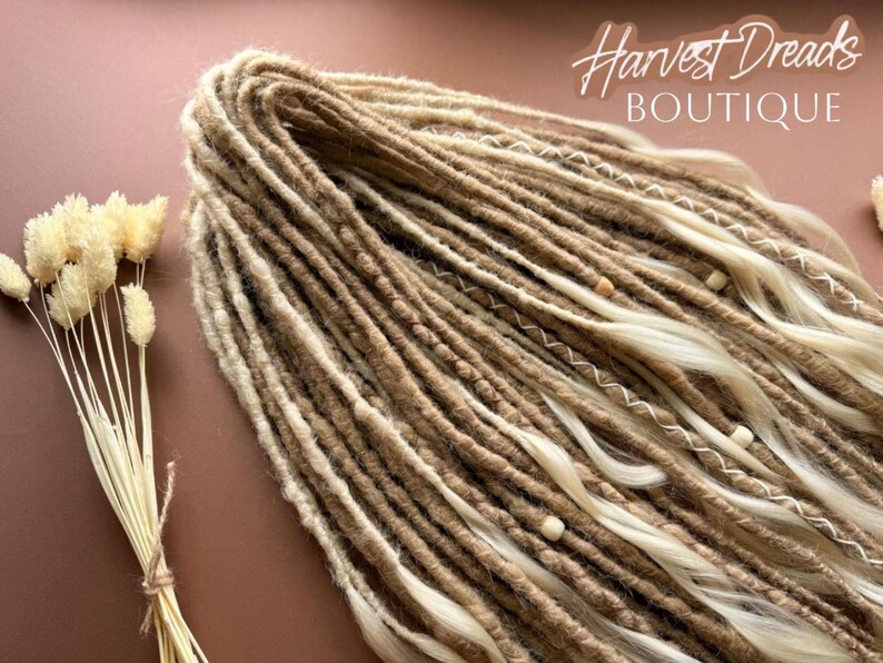 a collection of long, braided hair strands in various shades of brown and blonde, arranged on a pink background. There are also some dried flowers visible in the image.