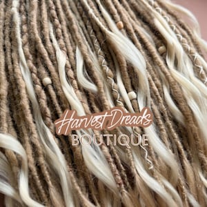 May include: Close-up of blonde and brown dreadlocks with wooden beads and white accents. The dreadlocks are wavy and have a natural look. The text "Harvest Dreads BOUTIQUE" is visible.