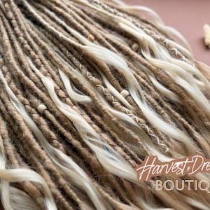 a close-up view of a collection of braided or woven hair strands, with some of the strands being white and others brown. The image appears to be a close-up of a hairstyle, possibly a braid or a woven braid. The background is a pinkish-brown color, which contrasts with the hair strands. There is also a small white flower or object visible in the top right corner of the image.