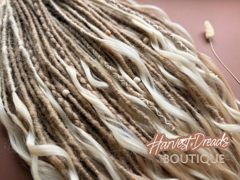 a close-up view of a collection of braided or woven hair strands, with some of the strands being white and others brown. The image appears to be a close-up of a hairstyle, possibly a braid or a woven braid. The background is a pinkish-brown color, which contrasts with the hair strands. There is also a small white flower or object visible in the top right corner of the image.