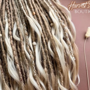 The image showcases a close-up view of a collection of braided and twisted hair strands, with a small white flower resting on the right side. The background is a pinkish-brown color, and there is text in the top right corner that reads "Harvest Dreads Boutique".