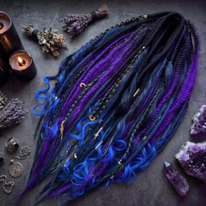 May include: A set of synthetic dreadlocks in shades of deep blue, royal blue, and vibrant purple. The hair extensions feature a mix of smooth, braided, and wavy textures, accented with small gold-toned charms, metallic beads, and thin gold wire wraps.