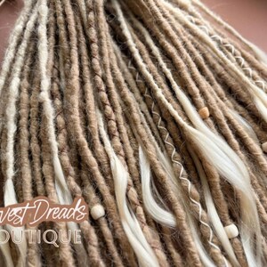 a close-up view of a collection of braided or twisted hair strands in various shades of brown and white, with small white beads or beads attached to some of the strands.