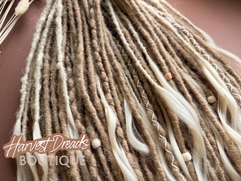 a close-up view of a collection of braided or twisted hair strands in various shades of brown and white, with small white beads or beads attached to some of the strands.
