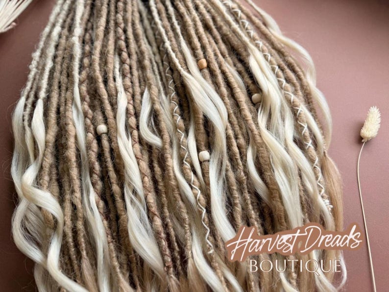 a close-up view of a collection of braided hair strands in various shades of brown and white, with small white beads scattered throughout. The image also includes a small white flower and the text "Harvest Dresses Boutique" in the background.