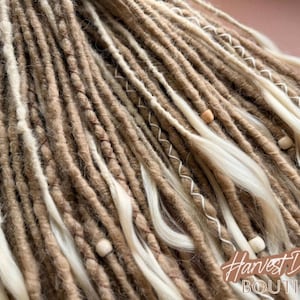 a close-up view of a collection of braided or twisted hair strands in various shades of brown and beige, with small white beads or beads attached to some of the strands.