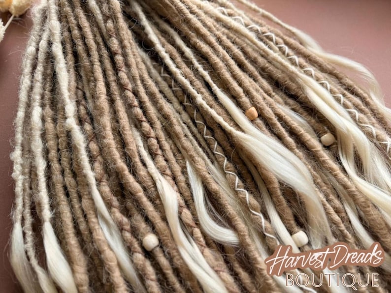 a close-up view of a collection of braided or twisted hair strands in various shades of brown and beige, with small white beads or beads attached to some of the strands.
