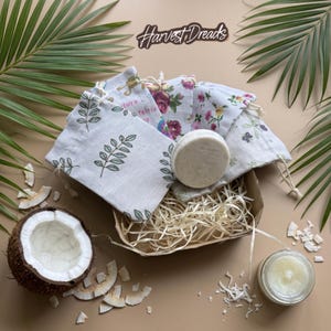 May include: A collection of small fabric drawstring pouches with various floral and leaf prints, a round white soap bar, a halved coconut, and a small glass jar of cream. The text Harvest Dreads is visible at the top of the arrangement.