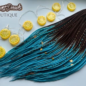May include: A set of synthetic dreadlocks featuring a dark brown to bright turquoise ombre color transition. The dreadlocks are adorned with decorative gold-toned leaf charms, beads, and intricate thread wraps. The text Harvest Dreads BOUTIQUE is visible.