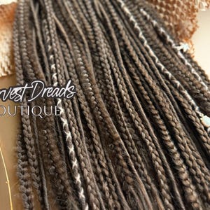 May include: Close-up of brown and light brown dreadlocks with white accents. The text "Harvest Dreads BOUTIQUE" is visible in the image. The dreadlocks are styled and appear to be handmade.