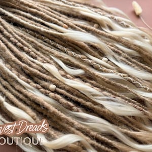 a close-up view of a collection of braided or twisted hair strands in various shades of brown and blonde, with small white beads or pearls scattered throughout.