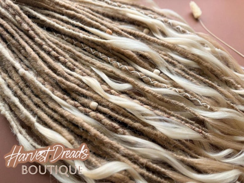 a close-up view of a collection of braided or twisted hair strands in various shades of brown and blonde, with small white beads or pearls scattered throughout.