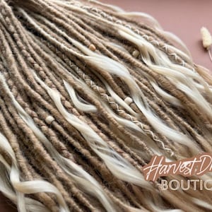 a close-up view of a collection of braided and twisted hair strands, with some beads and a small white flower visible among the strands.