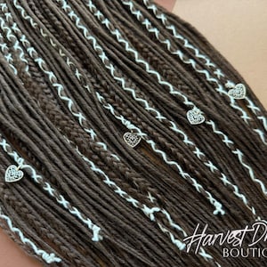 May include: Brown dreadlocks with white stitching and heart-shaped charms. The dreads are arranged diagonally, with the text "Harvest Dreads Boutique" in the bottom right corner. The dreads are a warm brown color.