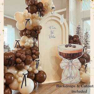 May include: A party decoration featuring a balloon arch in shades of brown and cream, accented with black ribbons. A cutout of a cocktail with coffee beans sits in front of a cream-colored archway. Text reads "A Tini Bit Older".