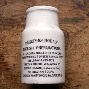 May include: White ceramic jar with black lettering advertising "Poulton & Noel's English Preparations" and listing various food products, including Belgravian Rolled Ox Tongues, Pressed Brisket of Beef & Spiced Beef, Belgravian Pate's, Turkey & Tongue, Veal & Ham, Oxford Brawn, Belgravian Soups, and Chicken Ham & Tongue Sausages.