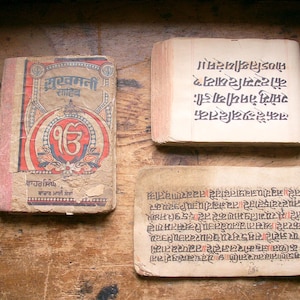 Puede incluir: Tres libros antiguos con cubiertas y páginas envejecidas y desgastadas. Un libro tiene una cubierta roja, blanca y azul con texto en idioma extranjero y un emblema circular. Los otros dos libros tienen texto manuscrito en idioma extranjero.