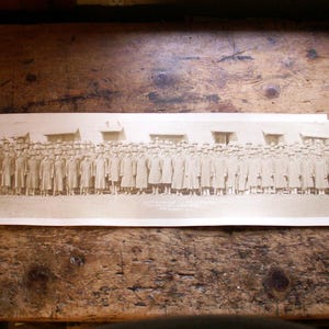 May include: A black and white photograph of a large group of people standing in a line. The people are all wearing uniforms and appear to be in a military setting.