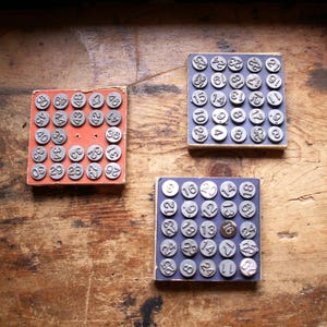 Peut inclure: Trois tampons de chiffres vintage sur des blocs de bois. Un bloc est rouge, les deux autres sont bleus. Chaque tampon a un numéro métallique circulaire. Les tampons sont disposés sur une surface en bois.