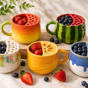 Pode incluir: Uma coleção de canecas de cerâmica coloridas com designs inspirados em frutas. Cada caneca apresenta um tema de fruta único, incluindo melancia, limão e morango, e é preenchida com frutas frescas. As canecas têm alças e recortes decorativos.
