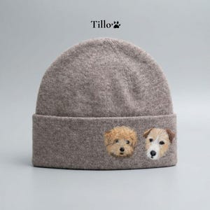 Puede incluir: Un gorro gris con caras de perro bordadas. El gorro tiene un borde doblado y la palabra "Tillo" encima. Los perros bordados incluyen un caniche y un terrier.