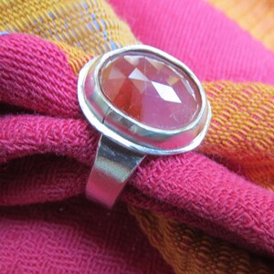 May include: A silver ring with a large, faceted, pink and red gemstone set in a bezel setting.