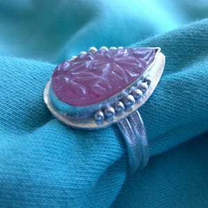 May include: A silver ring with a pink gemstone set in a leaf design. The ring is set with small silver beads around the edge of the stone.
