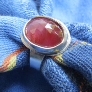 May include: A silver ring with a large, faceted, red gemstone set in a bezel setting.