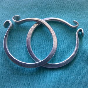 May include: Two silver hoop earrings with a hammered texture. The hoops are open and have a slightly curved shape.