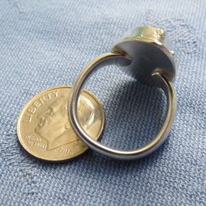 May include: A silver ring with a large, round, faceted gemstone. The ring is shown next to a US dime for size comparison.
