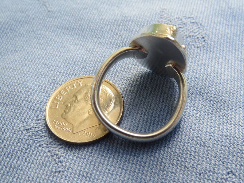 May include: A silver ring with a large, round, faceted gemstone. The ring is shown next to a US dime for size comparison.