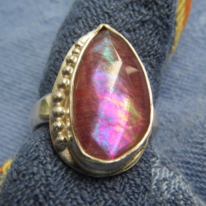 May include: A pearlescent pink gemstone ring with a silver band and beaded accents.