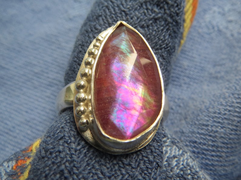 May include: A pearlescent pink gemstone ring with a silver band and beaded accents.