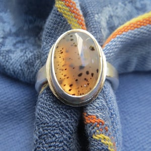 May include: A silver ring with a brown and white agate stone set in a silver bezel. The stone has a speckled pattern.