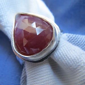 May include: A silver ring with a large, faceted, red gemstone in a teardrop shape.