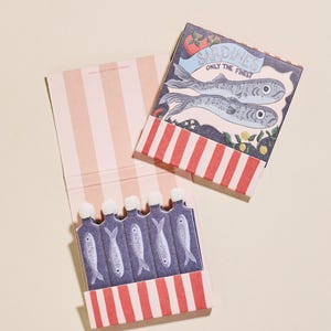 May include: Two sardine-themed matchboxes. One box is open, revealing five matchsticks with fish illustrations. The closed box features a sardine illustration with the text "Sardines Only The Finest". The boxes have red and white striped accents.