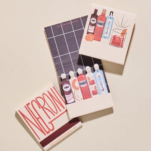 May include: Matchbooks with cocktail illustrations. One matchbook features the word "Negroni" in red. Other matchbooks depict bottles of liquor, cocktail glasses, and the words "Bitter", "Gin", and "Sweet Vermouth". A grid pattern is visible.