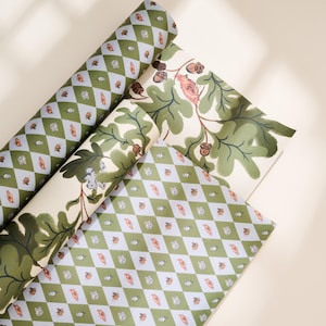 May include: Three rolls of wrapping paper featuring two distinct patterns. One pattern displays a green and white diamond argyle design with small orange and white bird motifs. The other pattern shows green oak leaves and brown acorns on cream.