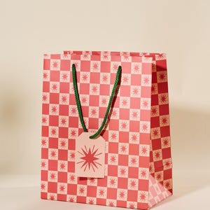 May include: A red and white checkered gift bag with green handles and a pink tag with a red starburst design.