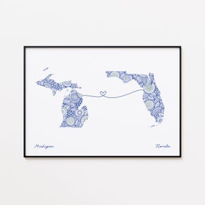 May include: A framed print featuring blue and white patterned outlines of the states of Michigan and Florida, connected by a line with a heart. The words "Michigan" and "Florida" are written below the states.