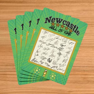 Puede incluir: Un montón de tarjetas verdes con el texto "Newcastle Hall of Fame" y múltiples firmas. Las tarjetas tienen un borde dorado alrededor de un rectángulo blanco lleno de firmas. Balones de fútbol y un trofeo en la parte inferior.