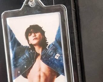 May include: Clear rectangular keychain with a silver metal ring. The keychain features a photograph of a person wearing a denim jacket and jeans. The person is shirtless, with arms raised. The background is a light color.