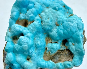 May include: A vibrant, textured mineral specimen featuring a striking turquoise-blue hue. The surface has a bubbly, organic appearance with areas of tan and brown. The overall shape is irregular, showcasing the natural formation of the stone.