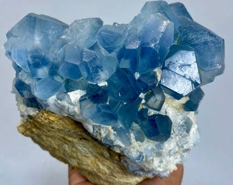 May include: A cluster of light blue celestite crystals on a beige and white matrix. The crystals have a geometric shape and are clustered together. The mineral specimen is a natural formation.