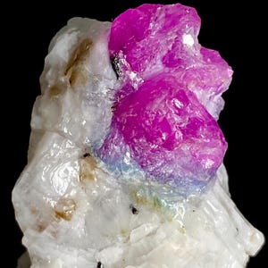 May include: A raw mineral specimen featuring a vibrant, translucent magenta crystal cluster embedded within a textured, opaque white matrix. The crystal displays a distinct color gradient, transitioning from deep pink at the top to a subtle blue hue at the base where it meets the white stone.