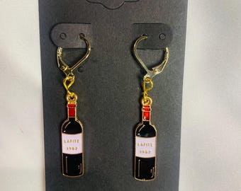 May include: Gold-tone leverback earrings featuring a black wine bottle design with red and white accents. The bottle design includes the text "LAFITE 1982". The earrings are displayed on a black card.