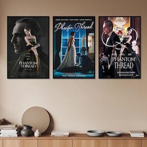Può includere: Sono esposti tre poster cinematografici incorniciati di "Phantom Thread". I poster presentano immagini di attori e attrici in abiti eleganti. Il titolo del film è ben visibile in un carattere stilizzato. I poster sono montati su una parete di colore neutro.